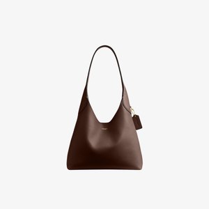 Sac bandoulière en cuir marron Coach avec une sangle unique et une petite étiquette suspendue sur fond blanc.
