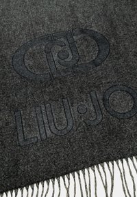 Šedý látkový šátek s texturovaným vzorem, na kterém je výrazně uvedeno jméno značky "LIU·JO" a má třásně na okrajích.
