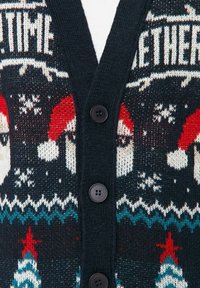 Cardigan buttonato di un blu navy scuro con facce di Babbo Natale lavorate a maglia, cappelli rossi e bianchi, fiocchi di neve e motivi di alberi di Natale in rosso, bianco e teal.