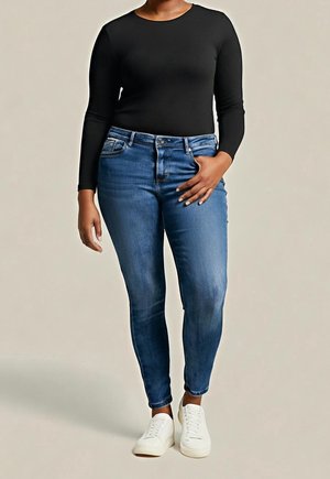 Person trägt ein schwarzes Langarmshirt, blaue Slim-Fit-Jeans und weiße Turnschuhe, steht mit einer Hand in der Nähe der Tasche.