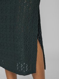 Σκούρο πράσινο, πλεκτό φόρεμα με σχέδια, γεωμετρικές σχισμές και πλαϊνή σχισμή. Διαθέτει υφή υφάσματος με χαλαρή ύφανση.