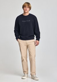 Sudadera azul marino con el logo "Polo Club", combinada con pantalones beiges y zapatillas ligeras. La tela parece suave con un diseño de corte relajado.