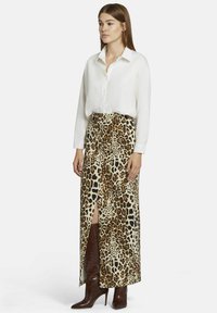 Jupe maxi en imprimé léopard avec une fente avant, associée à une chemise blanche à boutons et des bottes à talons marron. La texture semble lisse et légère.