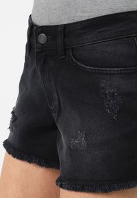 Mustat farkkushortsit, joissa on hapsutetut reunat, kulutettua ilmettä ja standardi viisi taskua -suunnittelu. Yleisesti rento istuvuus.