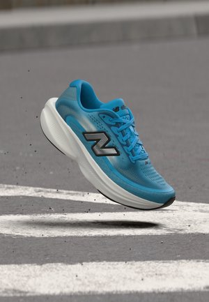 Μπλε αθλητικό παπούτσι New Balance με παχιά λευκή σόλα που αιωρείται πάνω από άσφαλτο με λευκές βαμμένες γραμμές.