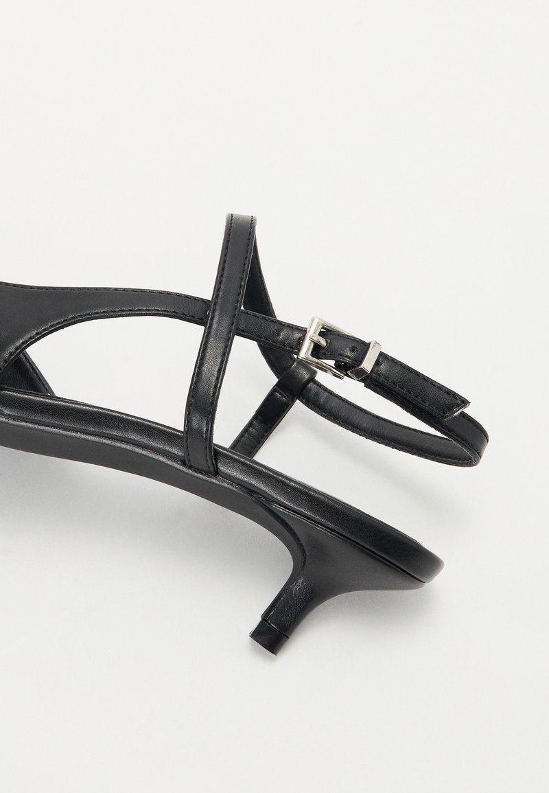 Sandal in pelle nera con tacco alto, dotata di sottili cinturini e una fibbia argentata. Presenta una punta affusolata e un tacco corto e curvo. Texture liscia.