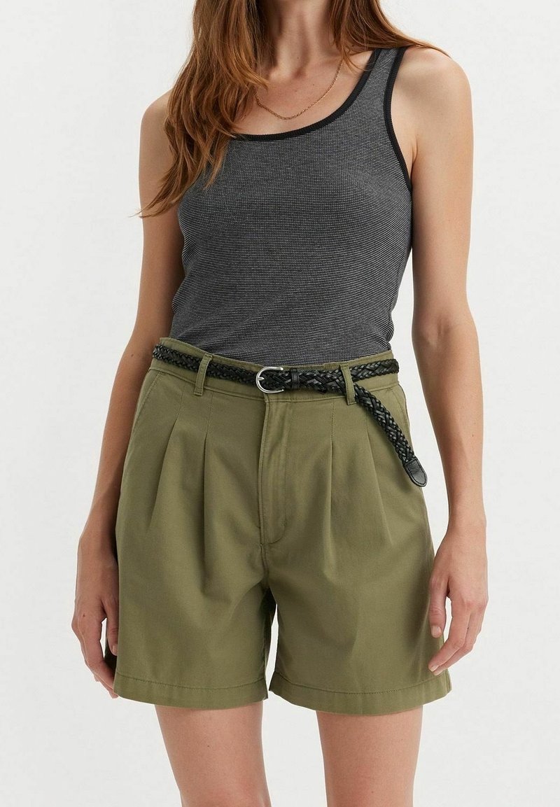 Femme portant un haut gris côtelé sans manches, rentré dans un short taille haute vert olive avec une ceinture noire tressée.
