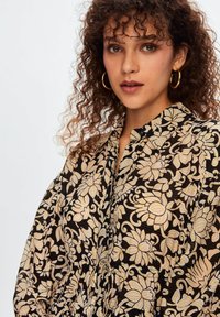 Blusa a fantasia floreale nera con fiori dorati e crema, dotata di colletto allacciato con bottoni e maniche larghe e gonfie.