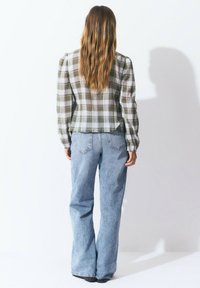 Chemise à manches longues à carreaux verts et blancs associée à un jean large bleu clair. La tenue présente un torse ajusté et une silhouette décontractée.