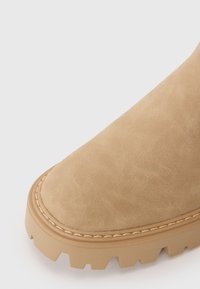 Bottine en suede tan avec un bout arrondi, des coutures renforcées et une semelle en caoutchouc épaisse et texturée, dotée d'un profond motif antidérapant.