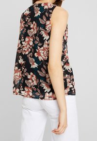 Top senza maniche floreale con base nera, caratterizzato da grandi fiori rosa e bianchi e accenti turchesi; tessuto leggero e drappeggiante, vestibilità comoda.