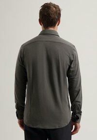 Langermet skjorte i mørkegrått stoff, med avslappet passform, ryggstykke detajler og knapplåser. Glatt tekstur med minimalistisk design.
