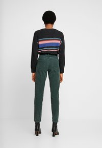 Svart och flerfärgad randig tröja med ribbad textur, tillsammans med gröna kordbyxor och svarta klackade ankelskor.