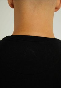 Svart bomulls t-shirt som visar halsringning och baksidan. Mindre sömdetalj synlig nära kragen. Slät textur med en figursydd passform.