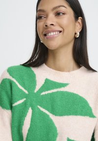 Grüner und cremefarbener Pullover mit großem Blattmuster, hergestellt aus weichem Strickmaterial mit Rundhalsausschnitt und strukturierter Oberfläche.