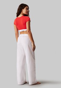 Crop top rouge à manches courtes avec une ceinture blanche Calvin Klein, associé à un pantalon de pyjama blanc à rayures larges, offrant une coupe décontractée.