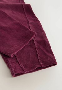Burgundské kordové kalhoty s ribovanou strukturou. Mají ohrnutý lem a viditelné stehy, které zdůrazňují měkký materiál.