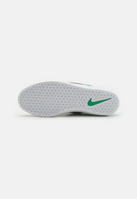 Fehér sneaker talp texturált mintával. Zöld Nike logóval rendelkezik. Tapadásra és stabilitásra tervezték. Kerek forma, gumiból készült.