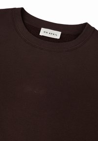 Sudadera marrón oscuro con cuello redondo, puños y dobladillo acanalados. Presenta un sutil logo bordado "Oh April" en la parte delantera. Textura suave.