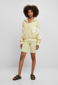 Ljusgul zip-up jacka med vita ränder, matchad med cykelshorts och svarta sandaler. Mjuk klädsel, avslappnad passform, avslappnad design.