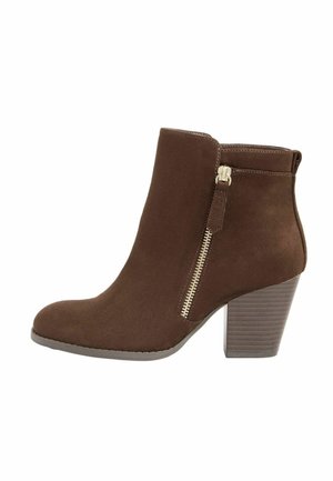 Botina din suede maro, cu vârf ascuțit, fermoar pe lateral și toc puțin înălțat. Botina are o textură netedă și accente minime.
