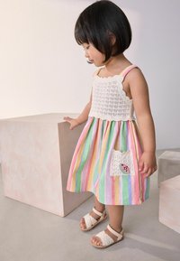 Robe rayée colorée dans des teintes pastel avec un corsage en crochet. Présente une poche latérale avec une application. Portée avec des sandales légères et texturées.