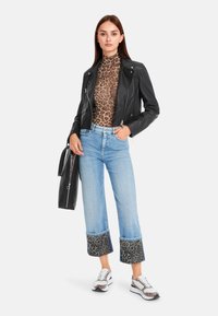 Black leather biker jacket, leopard print top, light blue cropped jeans with leopard print cuffs, and patterned sneakers.