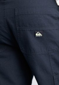 Navy cargobroek van een textuurstof, met meerdere zakken en een klein Quiksilver-logo op de achterkant.