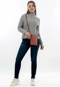 Maglione grigio a coste con collo alto, jeans blu scuro e sneakers bianche. Piccola borsa a tracolla marrone con cerniere. Outfit semplice e casual.