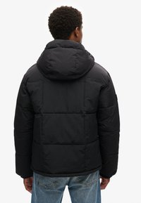 Giacca a vento nera con cappuccio, caratterizzata da un design trapuntato, polsini elasticizzati e una texture liscia. Vista da dietro.