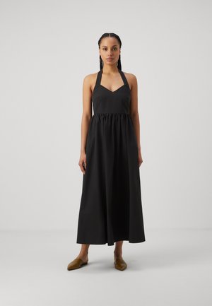 Svart halterneck-kjole med V-hals, samlet midje og lang flytende skjørt. Glatt stoff med minimal detaljer. Brukt med brune spisse leiligheter.