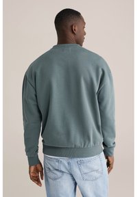 Sivo-modra jopa z okroglim izrezom, rebrastimi manšetami in pasom. Ima gladko teksturo in sproščen kroj. Nošena z svetlimi kavbojkami iz jeansa.