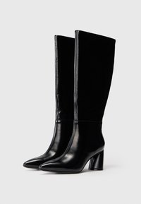 Botas negras hasta la rodilla, hechas de cuero suave, con punta afilada y tacón grueso. Presentan un diseño elegante sin adornos adicionales.