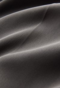 Zwarte stof met een gladde textuur, met subtiele golvingen en een lichte glans. Heeft een fijn, diagonaal streeppatroon.