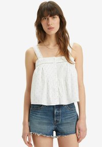 Hvid ærmeløs top med samlet front, dekorative knapper og blonde detaljer. Parret med slidte denimshorts.