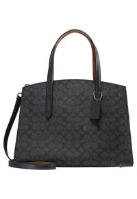 Sac à main structuré noir avec un motif texturé, doté de poignées en cuir marron et d'une bandoulière amovible, rehaussé par une petite étiquette.
