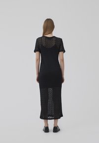 Abito nero a maglia con motivo a zigzag, maniche corte e una lunga parte trasparente che arriva fino a metà polpaccio.