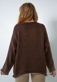 Brązowy sweter dziany o luźnym kroju, ribbowanej teksturze, opuszczonych ramionach i lekko zakrzywionym końcu. Widok z tyłu pokazuje długie rękawy.