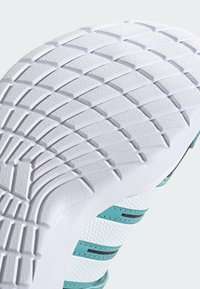 Semelle de basket blanche avec motif diamant texturé et dessus blanc avec des rayures bleu sarcelle et un détail en mesh hexagonal.