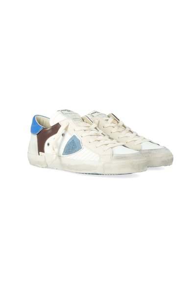 Sneaker basse color avorio con lacci beige, dettagli in pelle blu e marrone, un logo a scudo blu sul lato e suole testurizzate usurate.