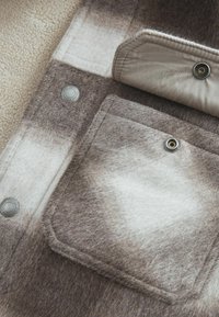 Brown and cream wool blend fabric featuring a large pocket, snap detail, and a soft, textured surface. Shades create a gradient effect.