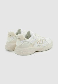 Zapatilla blanca que combina materiales de malla y ante, con forma redondeada, suela texturizada y un sutil detalle del logo en el talón.
