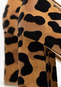 Escarpins à imprimé léopard avec un mélange de suède beige et d'accents texturés noirs, dotés d'un design de talon épais pour la stabilité et le style.