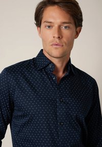 Granatowa koszula zapinana na guziki z drobnym, jasnoniebieskim wzorem paisley. Wykonana z gładkiej tkaniny, z klasycznym kołnierzykiem i czarnymi guzikami.