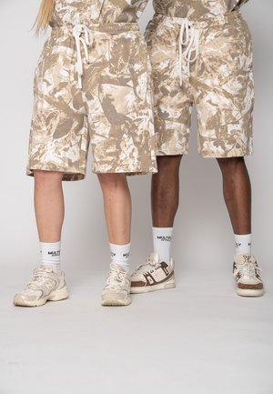 Two individuals wearing beige and white camouflage shorts, white socks with black text, and beige sneakers standing side by side.