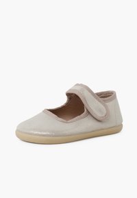 Zapato Mary Jane de color beige claro con textura brillante, correa de velcro y suela de goma flexible. Laterales abiertos y interior acolchado para mayor comodidad.