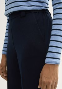 Marineblauwe plooibroek met een elastische tailleband, gecombineerd met een lichtblauw gestreept langemouwtop. De stof lijkt zacht te zijn met een gladde textuur.