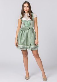 Green dirndl dress with a fitted bodice, lace-up front, and gathered skirt. Features floral accents and satin ribbon trim, paired with a white lace top.