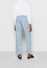 Pantalon en denim bleu clair à motif, coupe droite et taille haute, avec un logo imprimé. Associé à un sweat-shirt blanc court.