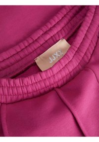 Suéter fucsia con un cuello texturizado y acanalado, y una etiqueta que muestra "JJXX". Tela suave con un acabado elástico, adecuada para uso casual.